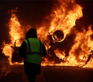 A demonstrator watches a burning car near the Champs-Elysees avenue during a demonstration Saturday, Dec.1, 2018 in Paris. (AP Photo/Kamil Zihnioglu)