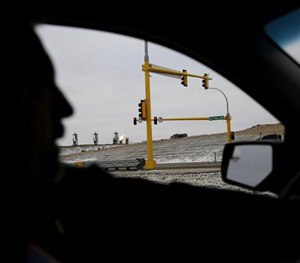 In this Tuesday, Dec. 16, 2014 photo, Watford City Police Chief Art Walgren passes oil wells in his police vehicle in Watford City, N.D.