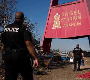 Two police officers, Eric Meier, right, and Curtis Bynum from the Anaheim Police Department's homeless outreach team walk through a homeless encampment set up outside Angel Stadium to hand out flyers about the community outreach day Tuesday, Dec. 19, 2017, in Anaheim, Calif.
