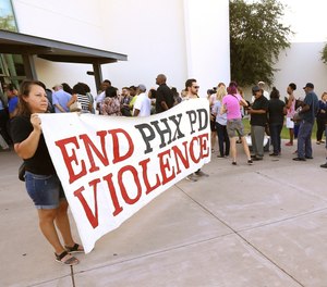 In this June 18, 2019, file photo, people line up near protesters outside a venue for a community meeting in Phoenix. (AP Photo/Ross D. Franklin, File)