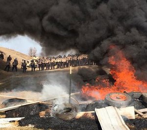 Demonstrators stand next to burning tires as armed soldiers and law enforcement officers assemble on Thursday, Oct. 27, 2016, to force Dakota Access pipeline protesters off private land where they had camped to block construction. (Mike McCleary/The Bismarck Tribune via AP)