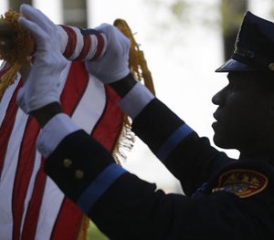 An officer rolls up a flag during a ceremony at the New York State Police Officers' Memorial in Albany, N.Y.
