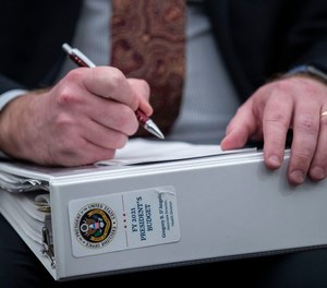 An aide holds a copy of the President's Budget for 2021, as Office of Management and Budget Acting Director Russell Vought testifies during a hearing of the House Budget Committee about President Trump's budget for Fiscal Year 2021, on Capitol Hill, Wednesday, Feb. 12, 2020, in Washington.
