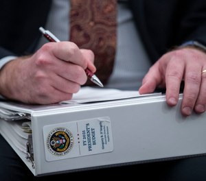 An aide holds a copy of the President's Budget for 2021, as Office of Management and Budget Acting Director Russell Vought testifies during a hearing of the House Budget Committee about President Trump's budget for Fiscal Year 2021, on Capitol Hill, Wednesday, Feb. 12, 2020, in Washington.