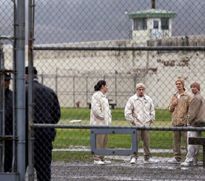 In this file photo, inmates mingle in a recreation yard in view of guards, left, at the Monroe Correctional Complex in Monroe, Wash.