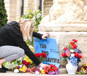 A woman adjusts a sign next to memorials to the two Anamosa State Penitentiary staff who were killed in an escape attempt.