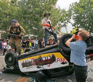 Armed protesters climb on a flipped over police vehicle Saturday, May 30, 2020, in Salt Lake City. (AP Photo/Rick Bowmer)