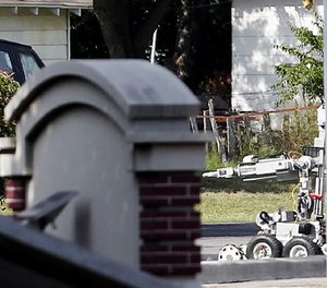 A bomb disposal robot inspects the area surrounding a armored van, top left of frame, during a stand off with a gunman barricaded inside the van, Saturday, June 13, 2015, in Hutchins, Texas.