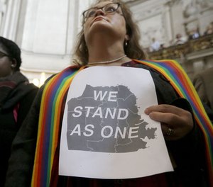 The Rev. Annie Steinberg-Behrman holds a sign while listening to speakers at a meeting at City Hall in San Francisco by city leaders and community activists to reaffirm the city's commitment to being a sanctuary city Monday, Nov. 14, 2016.