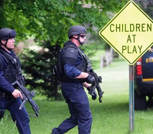Two law enforcement officers make their way across a lawn and onto Pleasant Street on Wednesday, June 10, 2015 in Dannemora, N.Y.
