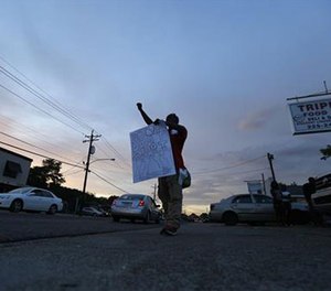 Troy Holliday, of Baton Rouge, holds a sign and gestures to passing motorists in honor of Alton Sterling, outside the Triple S Food Mart in Baton Rouge, La., Monday, July 11, 2016.
