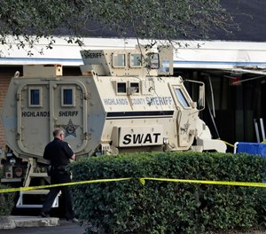 A Sebring, Fla., police officer stands near a Highlands County Sheriff's SWAT vehicle that is stationed in front of a SunTrust Bank branch, Wednesday, Jan. 23, 2019, in Sebring, Fla.