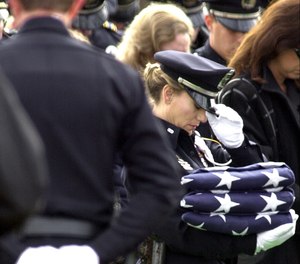 Police honor guard member Naya Pope bows her head while holding three folded American flags for intended for the family of slain Irving, Texas, police officer Aubrey Hawkins during burial services in Irving, Thursday, Dec. 28, 2000.