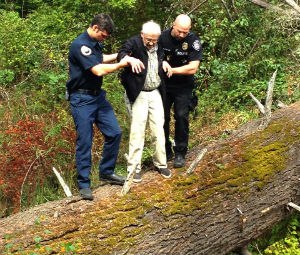 A firefighter and police officer help the man off of the fallen tree he had climbed.