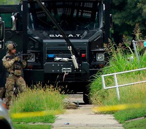 A police officer in tactical gear stands positioned near an Illinois State Police S.W.A.T. vehicle outside a building on 42nd Street near Van Buren Avenue, on Friday, Aug 23, 2019, in East St. Louis, Ill., after a state trooper was shot while serving a warrant at the address. (Christian Gooden/St. Louis Post-Dispatch via AP)