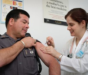 This CDC shows a law enforcement officer receiving a vaccination from a public health nurse.