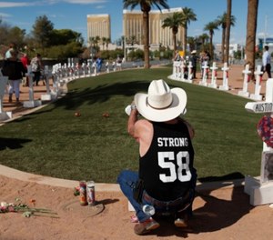 Jim Strickland, of Oroville, Calif., writes a message on a cross at a makeshift memorial for victims of the Oct. 1, 2017, mass shooting in Las Vegas, Sunday, Sept. 30, 2018, in Las Vegas.