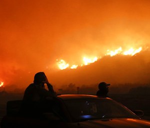 Two spectators watch as a wildfire burns along the 101 Freeway. (Photo/AP)