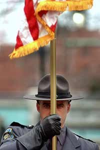 Department of Corrections Officer John Bray stands at attention as he and fellow correction officers present the flags while victims of violence plant flowers at a ceremony held as part of National Crime Victims' Rights Week in R.I. (AP photo)