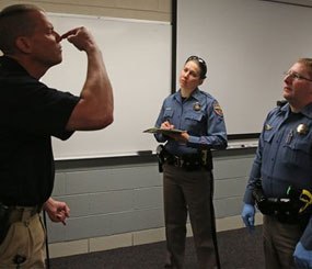 Simulating a roadside investigation of a potentially intoxicated driver, Colorado State Trooper Sgt. David Blatner, left, pretends to be high and struggling to touch his nose with his eyes closed as he trains troopers Carrie Jackson, center, and Toby Cox in a several week long Drug Recognition Expert class.