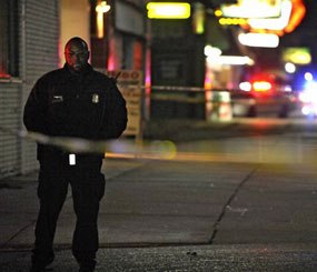 In this Wednesday, Nov. 6, 2013 file photo, a Detroit Police officer stands guard behind barrier tape at the scene of a shooting which left three dead at a barbershop in Detroit.