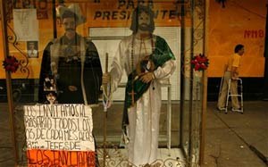 A man walks past a street shrine with two fully-dressed manequins representing Jesus Malverde, the hero or