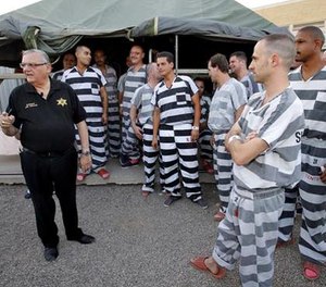 In this , June 23, 2012, file photo, inmates gather next to Maricopa County Sheriff Joe Arpaio as he walks through a Maricopa County Sheriff's Office jail called 