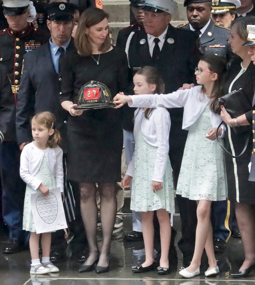 Shannon Slutman holds the fire helmet of her late husband, U.S. Marine Corps Staff Sergeant and FDNY Firefighter Christopher Slutman, while standing with their children as his casket leaves St. Thomas Episcopal Church, Friday April 26, 2019, in New York. (AP Photo/Bebeto Matthews)