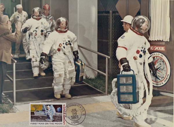 Astronaut Rescueman Bill Killen escorts Apollo 15 crewmembers from their quarters in the Manned Spacecraft Operations Building en route to Launch Complex 39. This NASA photograph is unique in that it shows a 10 cent Moon Landing Stamp and was hand-canceled at the Kennedy Space Center Post Office shortly after liftoff.