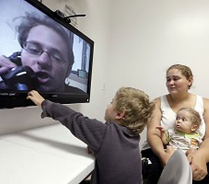 In this photo taken on Tuesday, May 5, 2015, inmate Jesse Cole is shown on a television screen as his son William, 4, center, reaches to touch the screen while his mother, Edna, holds 8-month-old Jesse James, during a video visitation with at the Fort Bend County Jail, in Richmond, Texas.